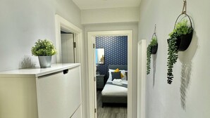 A narrow hallway with a kitchenette on the left, a bed with a blue patterned headboard in the center, and a radiator on the right.