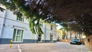 A paved driveway leading to a building with a grey facade and green window frames.