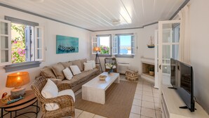 A living room with a sofa, coffee table, TV, and open windows. - The Villa Evita in Spetses. Stunning view, private pool and daily maid service. (Spetses Island)