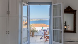 Eine offene Tür, die auf einen Balkon mit Meerblick führt, mit einem Tisch, einem Stuhl und einem Spiegel an der Wand.
