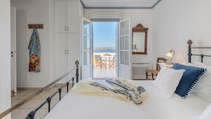 Ein Schlafzimmer mit einem Bett, einem Nachttisch, einem Sessel und Blick ins Freie.