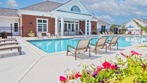 A pool area with lounge chairs, a brick building with large windows, and a clear blue sky. - New Albany 2BR | 2-Car Garage | Walk to Dinner (Columbus)