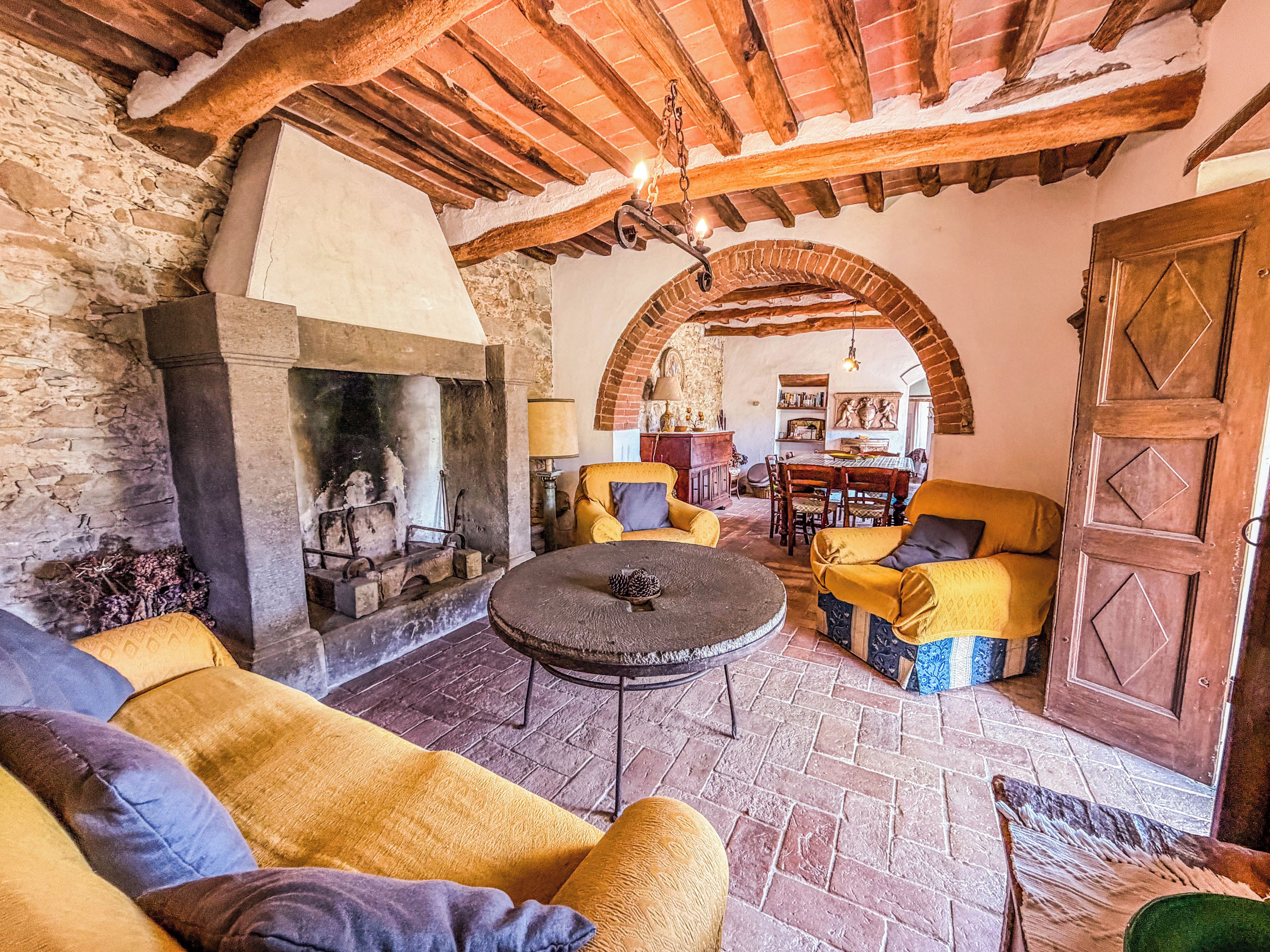 A rustic interior with a stone fireplace, wooden beams, and yellow upholstered furniture.