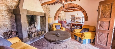 A rustic interior with a stone fireplace, wooden beams, and yellow upholstered furniture.