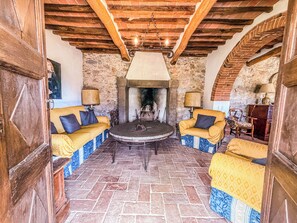 A rustic interior with a stone fireplace, wooden beams, and a round table with chairs.