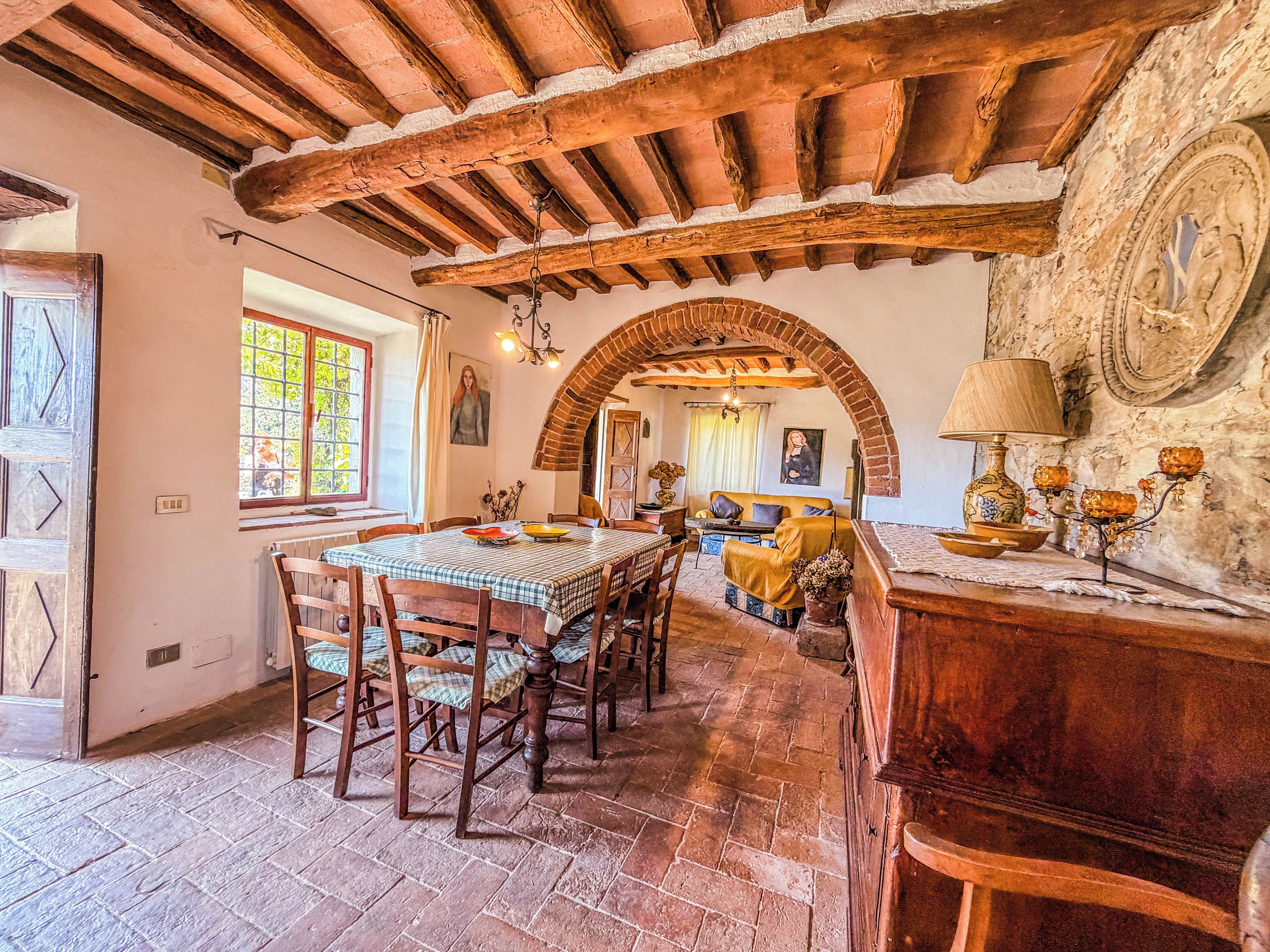 A rustic dining area with a wooden table and chairs, a brick fireplace, and a stone wall with a circular window.