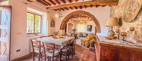 A rustic dining area with a wooden table and chairs, a brick fireplace, and a stone wall with a circular window.
