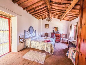 Ein Schlafzimmer mit Holzboden, einem Bett mit Kopfteil, einem Schminktisch, einem Spiegel und einem Fenster mit Vorhängen.