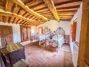 A rustic bedroom with a wooden ceiling, two beds with ornate headboards, a wooden chest, and a window with a view.