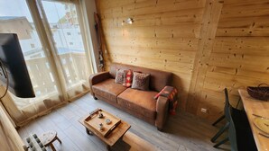 A cozy living room with a brown leather sofa, wooden walls, a TV mounted on the wall, and a wooden coffee table with a tray. - Center Val Thorens apartment 4 people (Les Belleville)