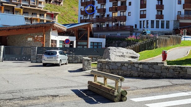 A multi-story hotel with balconies, a parking area, and a mountainous backdrop. - Center Val Thorens apartment 4 people (Les Belleville)