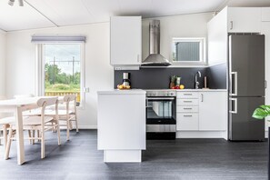 Une cuisine moderne avec des meubles blancs, un four encastré, un réfrigérateur en acier inoxydable et un coin repas comprenant une table et des chaises en bois.