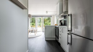 A modern kitchen with white cabinets, stainless steel appliances, and a large window providing a view of the outdoors. - Private Chalet (Skelleftea)