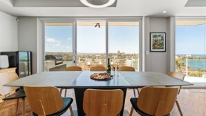 Un espace repas comprenant une grande table, six chaises, un barbecue et une vue sur la ville et la mer.