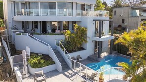 Une maison moderne à plusieurs étages, dotée d’une piscine, d’un espace salon extérieur et d’un escalier menant à un balcon.