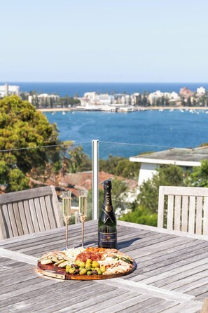 A wooden table with a charcuterie board, two glasses, and a bottle of Moët & Chandon wine, overlooking a coastal cityscape. - Seabreeze - Balgowlah Heights Beach House w/ Pool (Balgowlah Heights)
