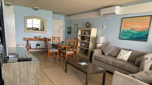 Ein Wohnzimmer mit Sofa, Couchtisch, Esstisch mit Stühlen und Bücherregal.