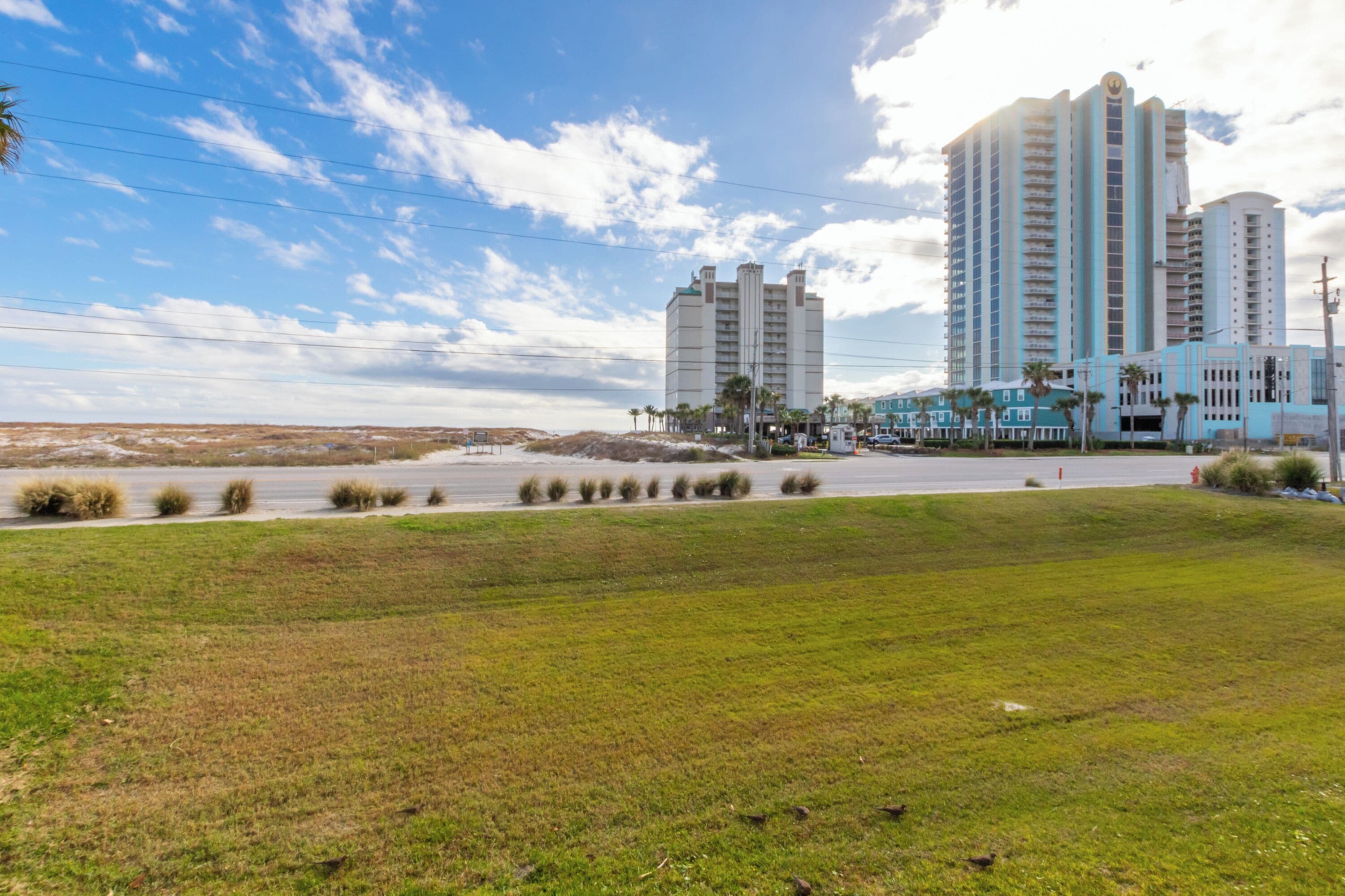 A coastal hotel with multiple high-rise buildings, a parking lot, and a grassy area.