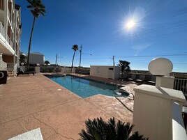 Une piscine entourée d’un ciel d’un bleu éclatant, de palmiers et d’un bâtiment doté de balcons.