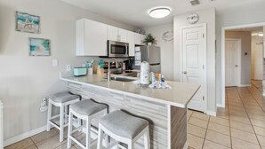 Een moderne keuken met een centraal kookeiland, barstoelen, een magnetron, een koelkast en een spoelbak.