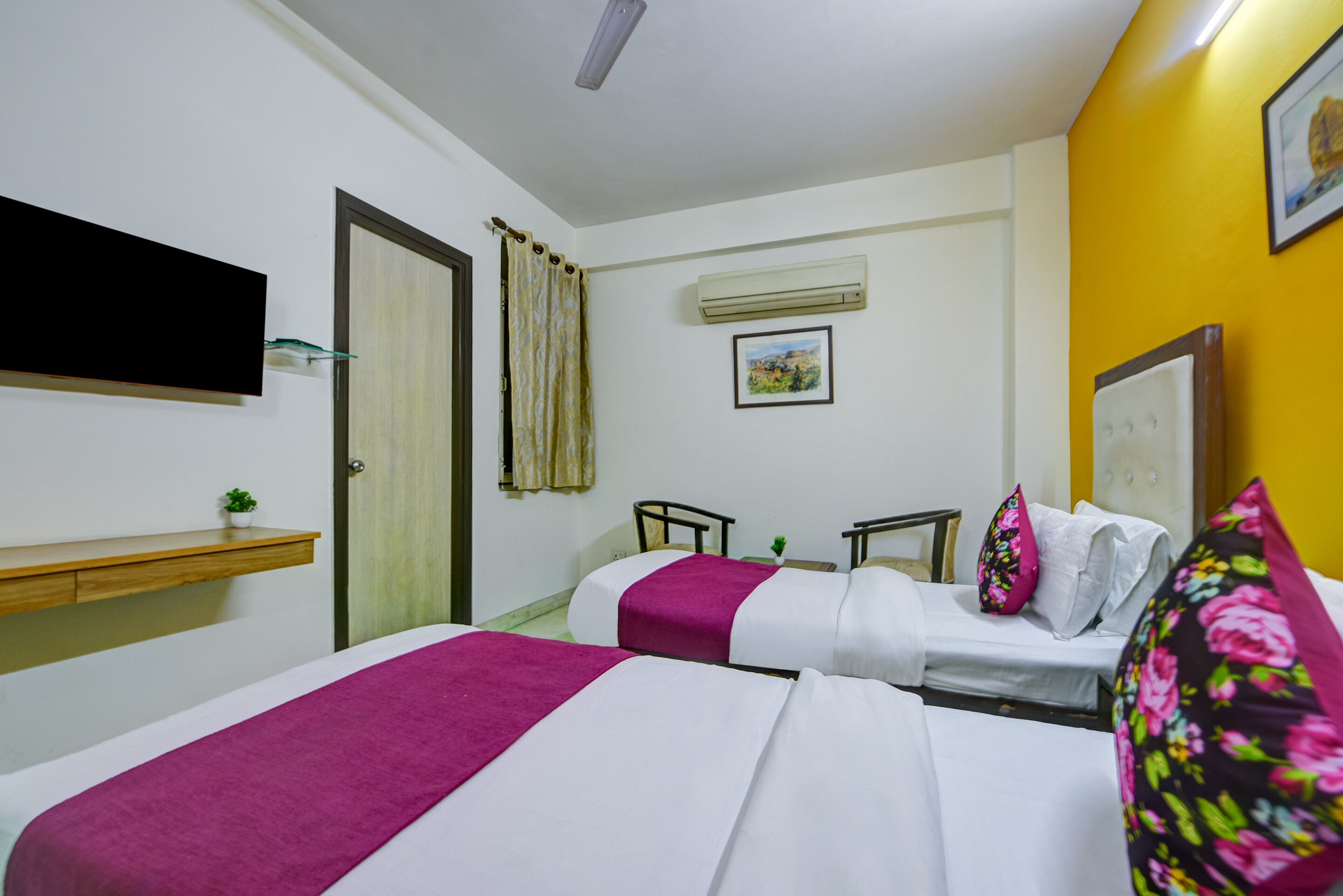 Habitación de hotel con dos camas, un televisor montado, un equipo de aire acondicionado y una planta pequeña.