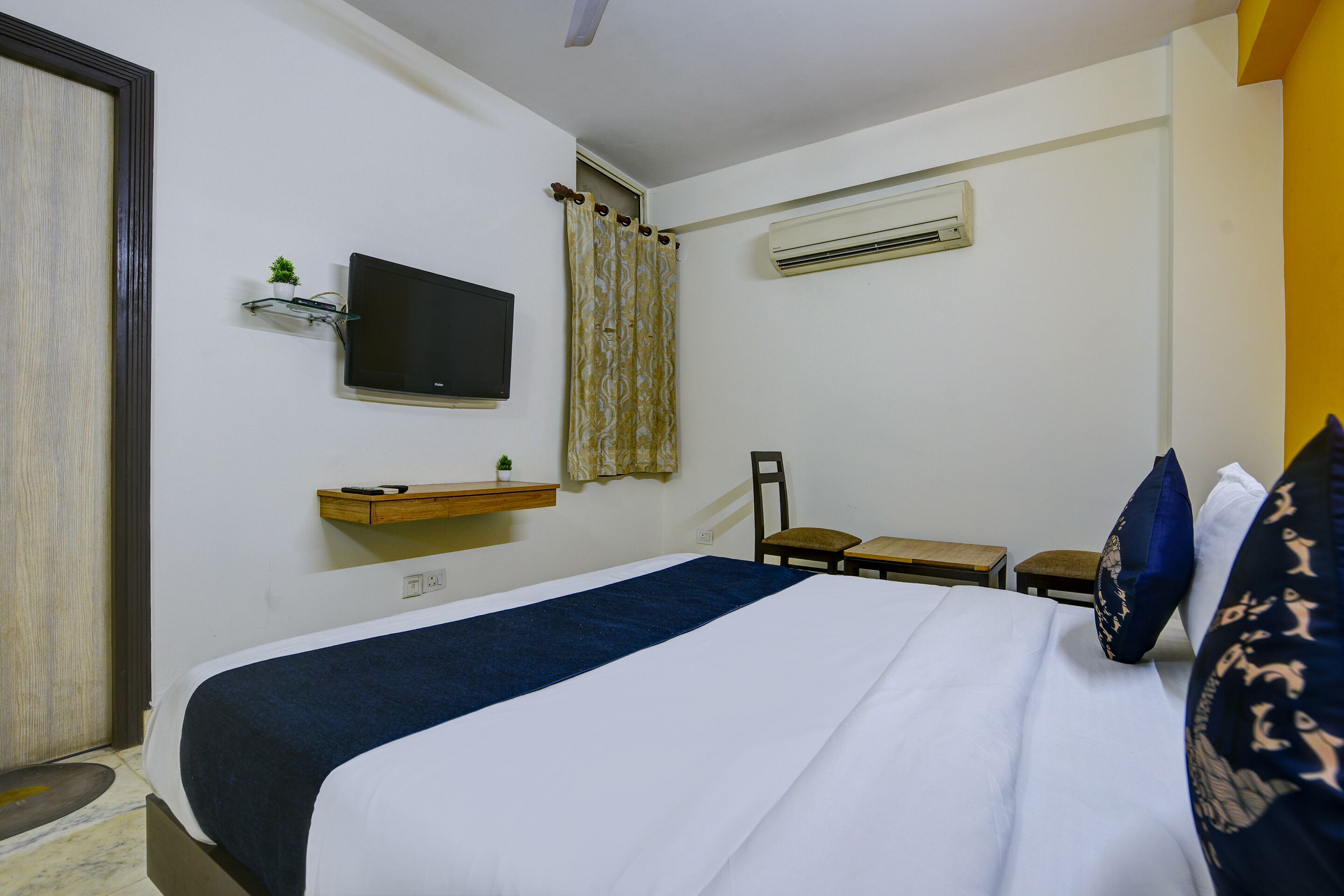 Une chambre d’hôtel équipée d’un lit, d’une télévision, d’une petite table, d’une chaise et d’un appareil de climatisation.