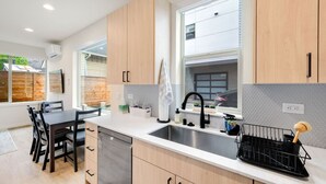 A modern kitchen with light wood cabinets, a stainless steel sink, and a dining area with a table and chairs. - Urban Roosevelt/Greenlake Getaway (Seattle)