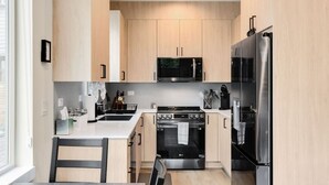A modern kitchen with light wood cabinets, a stainless steel refrigerator, a microwave, an oven, and a sink. - Urban Roosevelt/Greenlake Getaway (Seattle)