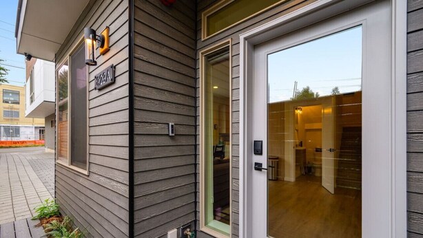 A building with a gray exterior, a glass door entrance, and a small outdoor area with plants. - Urban Roosevelt/Greenlake Getaway (Seattle)