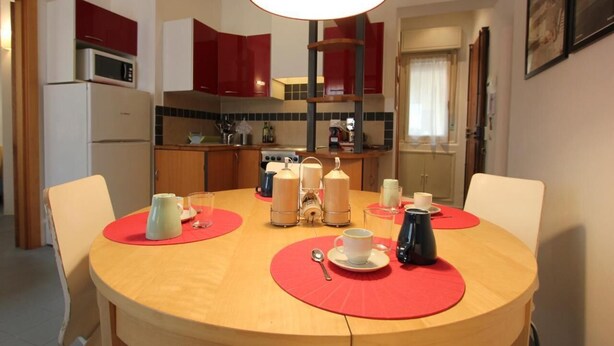 A dining area with a round table, red placemats, and various tableware. - Barbadori Suite (Florence)