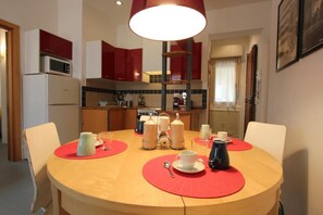 Zona pranzo con tavolo rotondo, sottopiatti rossi e vari utensili da tavola.
