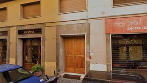 A building with a closed wooden door, a visible shop sign, and a parked car. - Barbadori Suite (Florence)