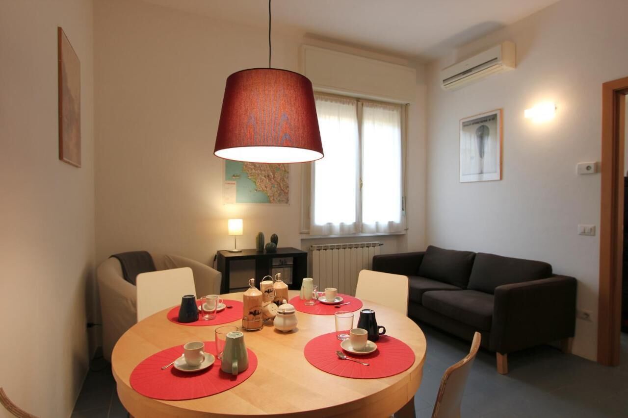 Ein Essbereich mit einem runden Tisch, gedeckt für vier Personen, einer roten Pendelleuchte und einer braunen Couch im Hintergrund.