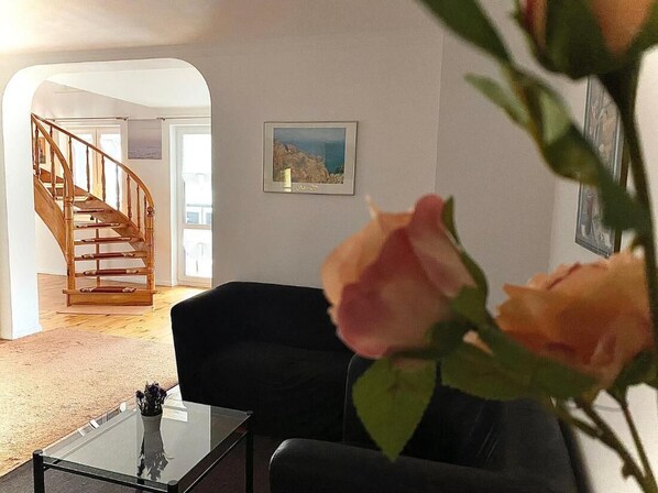 A living room with a staircase, a black sofa, a glass coffee table, and a framed picture on the wall. - Penthouse in the old Citycenter (Kolobrzeg)