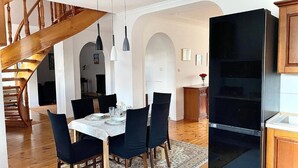 A dining area with a wooden staircase, a black refrigerator, and a white wall with framed pictures. - Penthouse in the old Citycenter (Kolobrzeg)