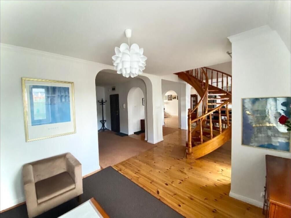 Amplia sala de estar con suelo de madera, una escalera y un candelabro.