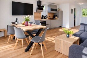 A modern kitchen with a flat-screen TV, a dining area with a wooden table and chairs, and a living room with a sofa and a coffee table. - Holiday Apartment 903 in Winterberg – The Accommodation for Large Families (Winterberg)
