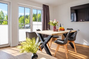 Un comedor con mesa de madera, sillas negras, un florero y una cesta de frutas.
