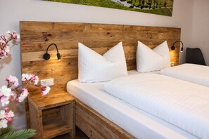 Un dormitorio con cabecera de madera, dos camas blancas, lámparas de noche y una mesita de noche de madera.