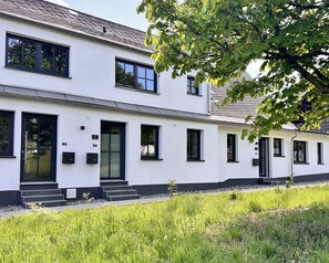 A two-story white building with black-framed windows and doors, a visible number plate, and a small set of steps leading to the entrance.