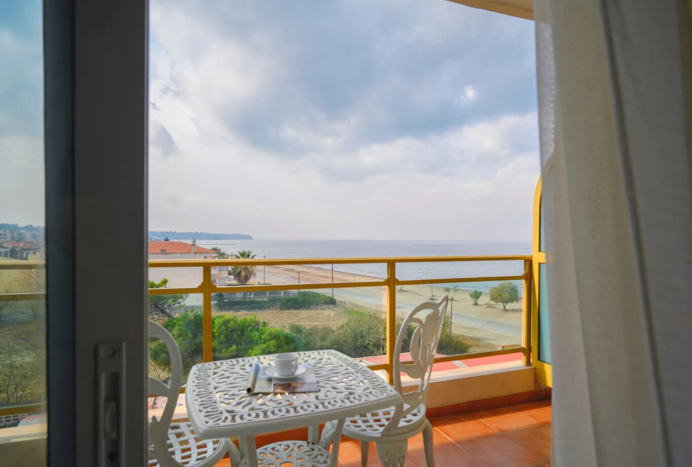 Uma varanda com mesa e cadeiras, com vista para uma área costeira com edifícios e uma estrada.