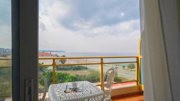 Uma varanda com mesa e cadeiras, com vista para uma área costeira com edifícios e uma estrada.