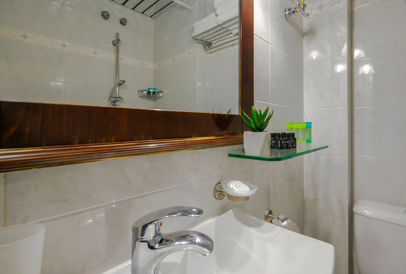 Ein modernes Badezimmer mit einem weißen Waschbecken, einer Glasablage für Pflegeprodukte, einer Duschkabine und einem hölzernen Waschtisch.