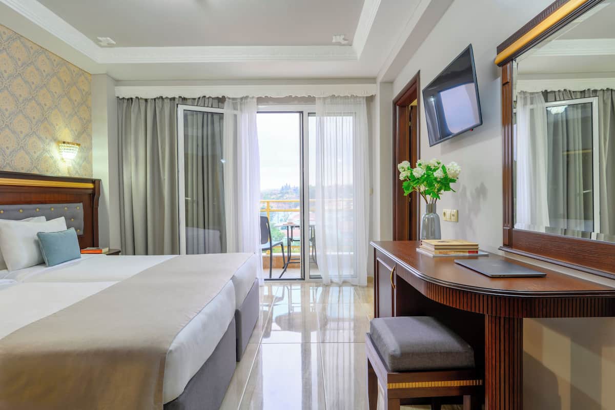 A hotel room with a large bed, a desk with a chair, a television, and a view of the outdoors.