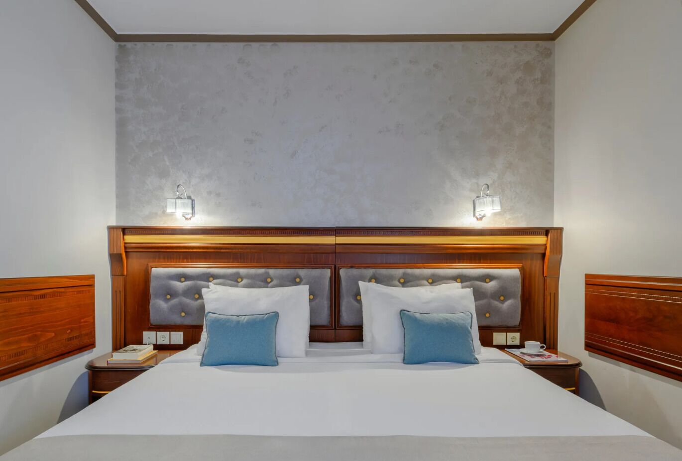Una cama doble con cabecera de madera, dos mesitas de noche y dos lámparas de pared.