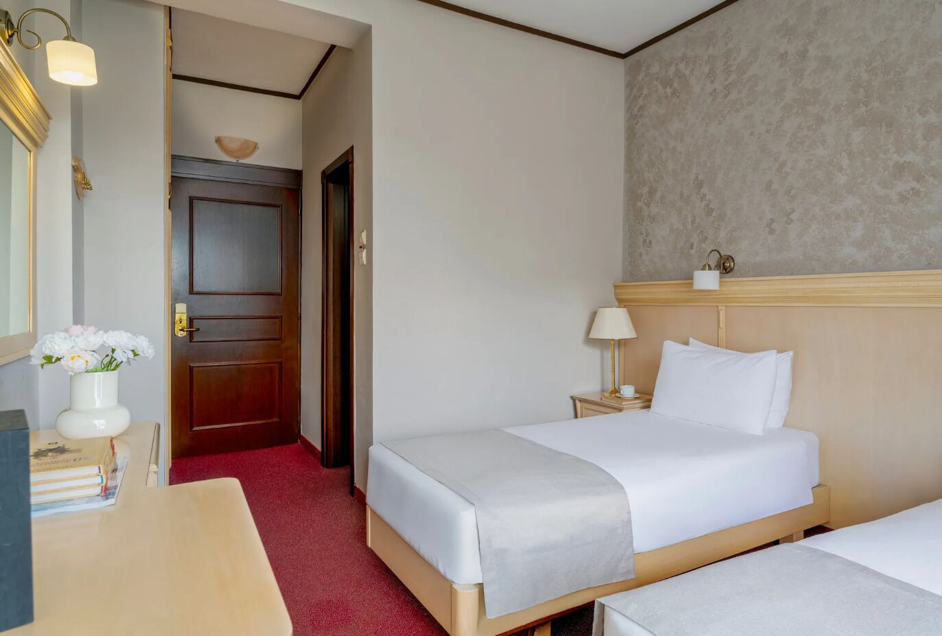 Une chambre d’hôtel avec deux lits, une porte en bois, une petite table de chevet avec une lampe et un miroir.