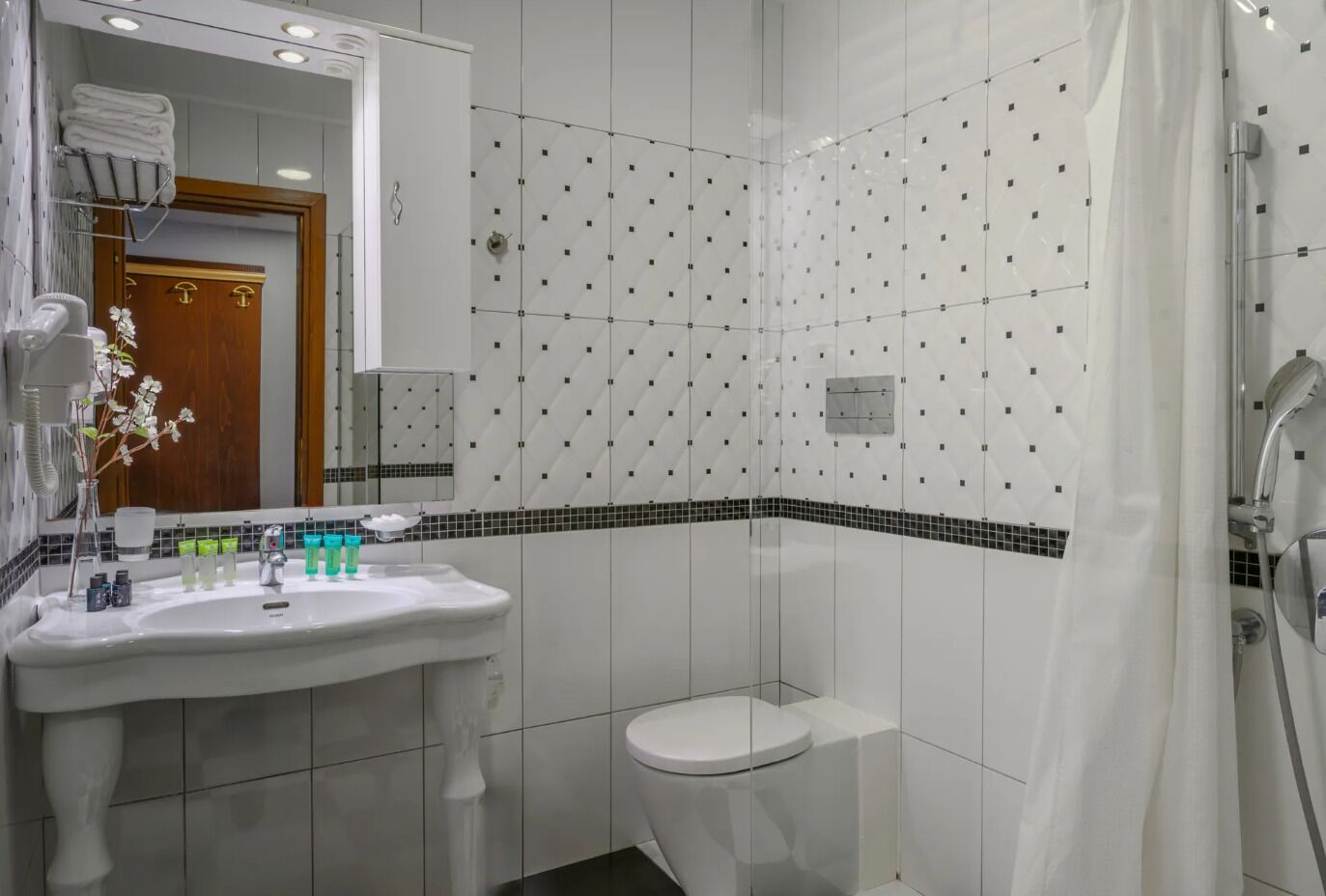 A modern bathroom with a white sink, mirror, and toilet. There is a shower curtain and a towel rack visible.