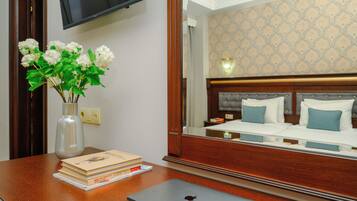 A hotel room with a wooden desk, a laptop, a vase with flowers, and a bed with blue pillows.