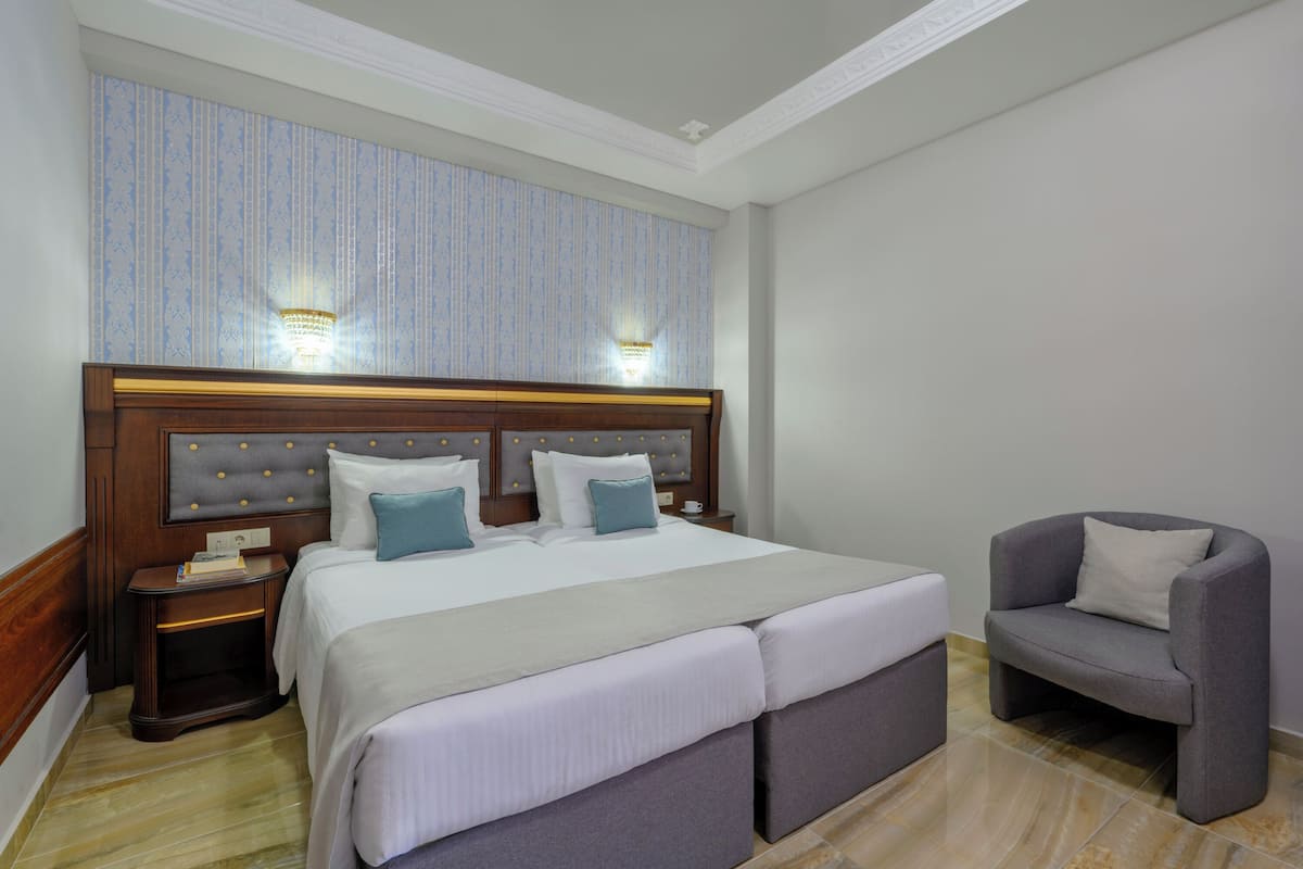A hotel room with a large bed, two bedside tables, a chair, and a wall-mounted light fixture.