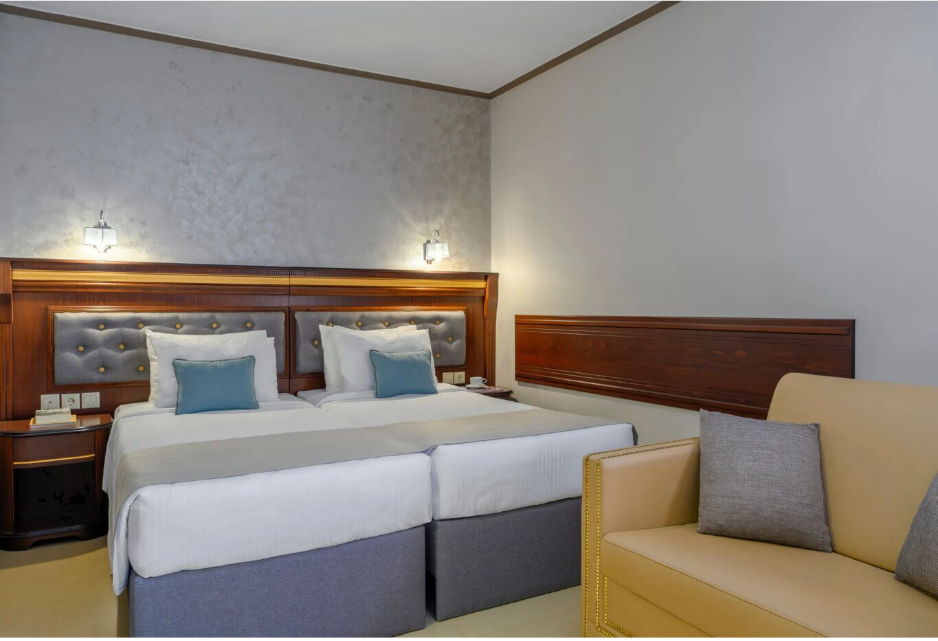 Habitación de hotel con una cama grande, dos mesitas de noche, un rincón de noche, un sofá y un cabecero con iluminación integrada.